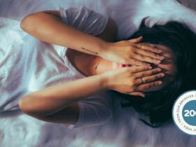 Woman lying on the floor practicing restorative yoga with her hands over her face