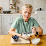 woman eating yogurt with blueberries in kitchen