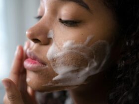 Young woman with closed eyes rubbing foamy soap on her cheeks