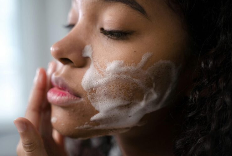 Young woman with closed eyes rubbing foamy soap on her cheeks