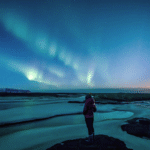 Woman standing beneath the northern lights on winter solstice contemlating weekly horoscope for December 21-27, 2025