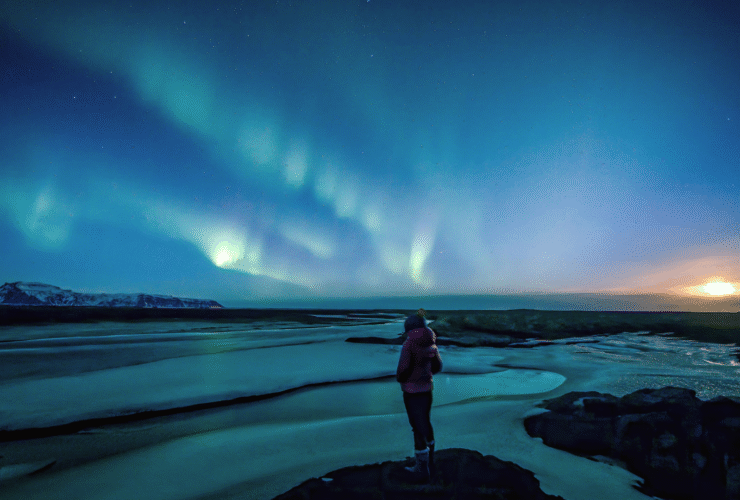 Woman standing beneath the northern lights on winter solstice contemlating weekly horoscope for December 21-27, 2025