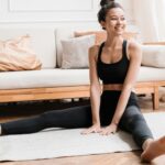 Woman smiling sitting with her legs in a V shape on yoga mat.