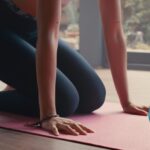 Woman kneeling on a yoga mat with her hands beneath her shoulders about to lift herself into Lolasana or Pendant Pose