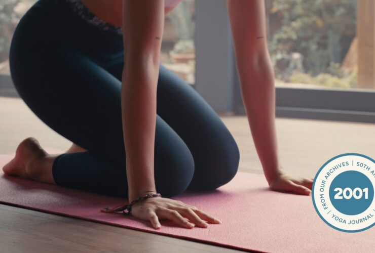 Woman kneeling on a yoga mat with her hands beneath her shoulders about to lift herself into Lolasana or Pendant Pose
