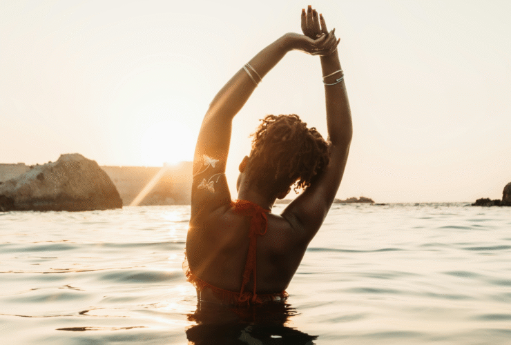 Woman with curly hair pulled back with a tie while she's in the sea and stretching her arms upward