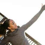 Image of woman outside stretching her arm toward the bright sky.