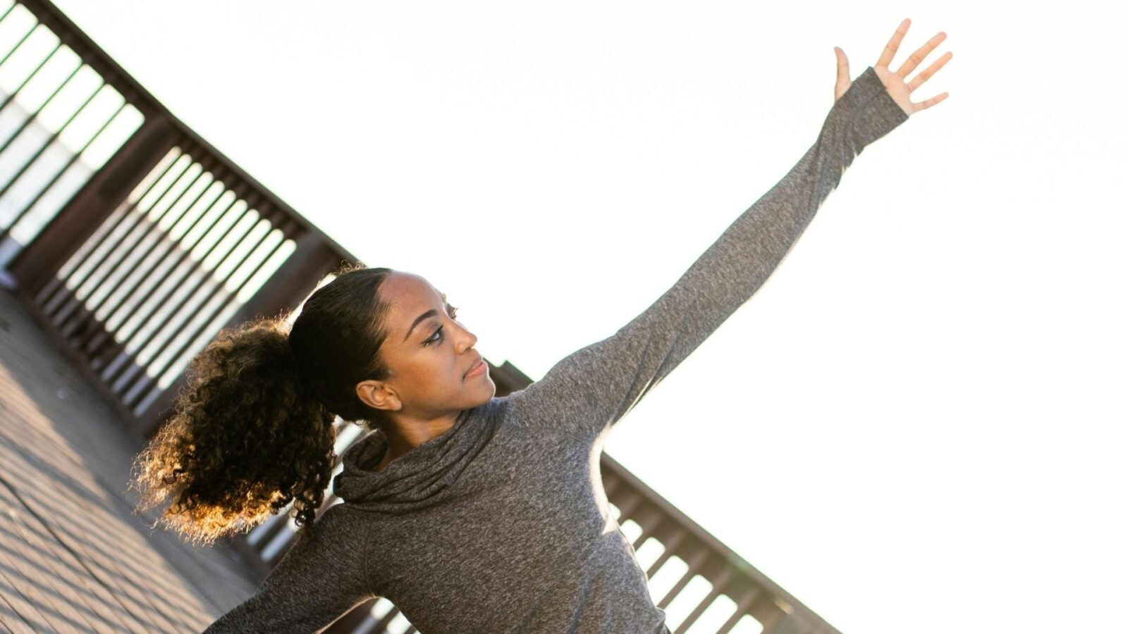 Image of woman outside stretching her arm toward the bright sky.