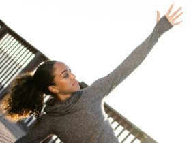 Image of woman outside stretching her arm toward the bright sky.