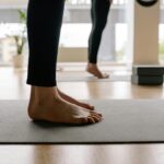 Close-up of people's feet standing on a black yoga mat.