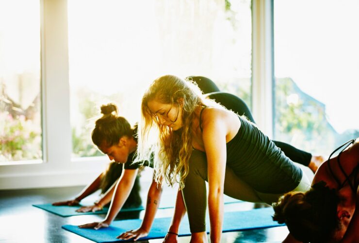 Students in a yoga class transition from Down Dog to Low Lunge