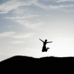 Woman jumping in the air while hiking and contemplating her weekly horoscope