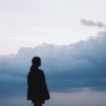 Woman staring off into a cloudy, overcast day during winter while contemplating the weekly horoscope for February 1-7, 2026