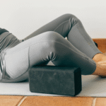 A person on a yoga mat using yoga props including a block and a bolster