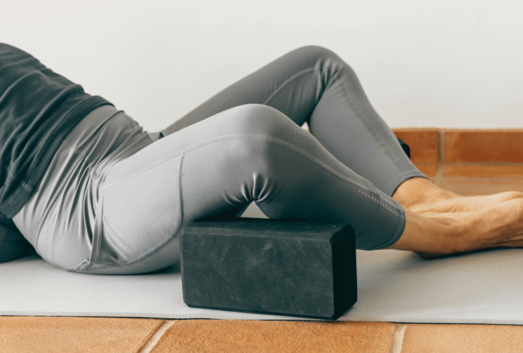 A person on a yoga mat using yoga props including a block and a bolster