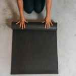 A woman crouching on the ground rolling up one of the best yoga mats