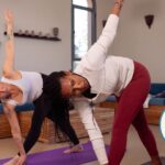 Two women practicing revolved triangle pose at home.