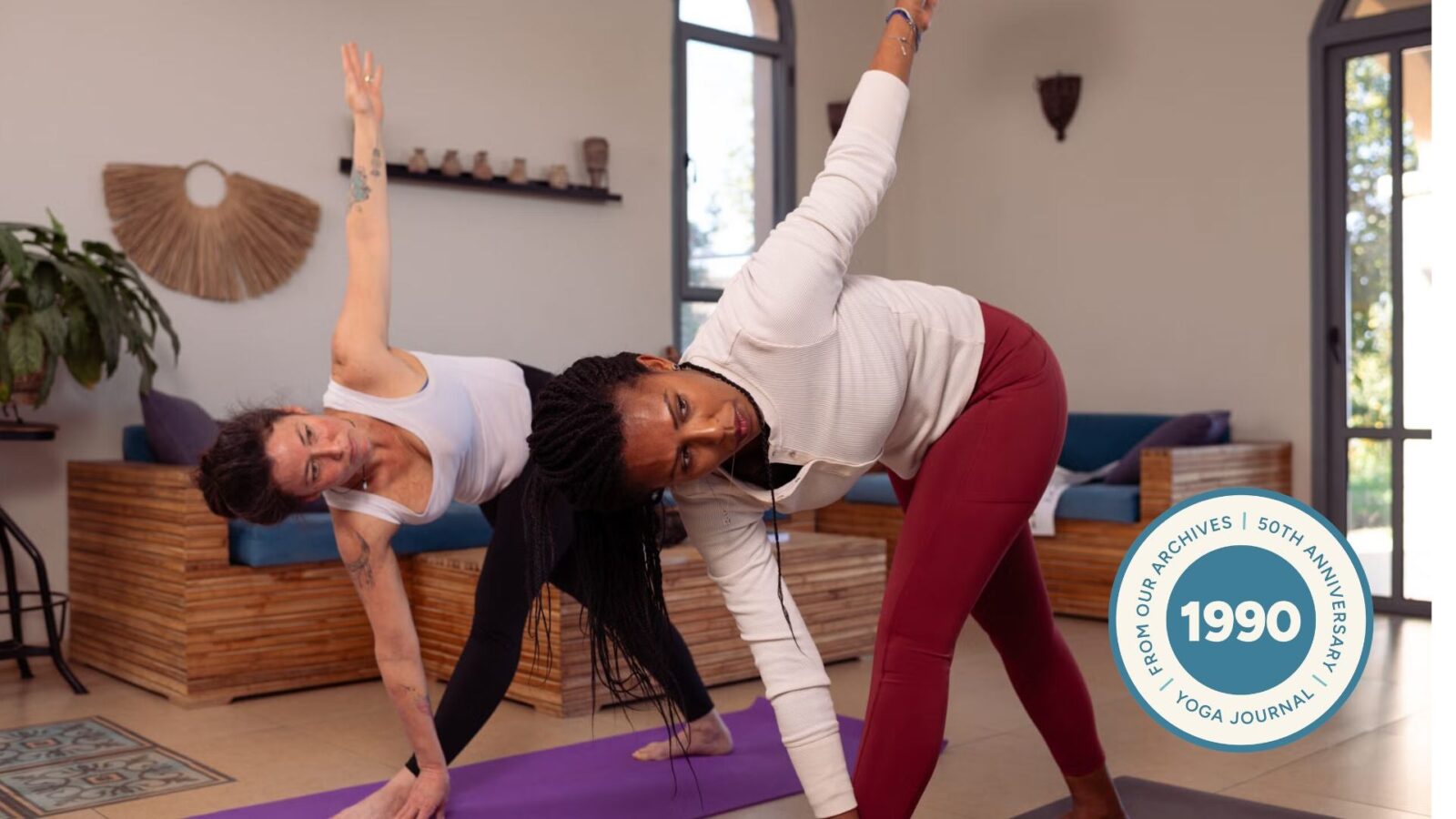 Two women practicing revolved triangle pose at home.