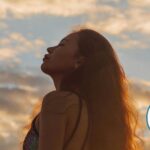 Silhouette of a woman who's standing outside during sunset with a blue-pink sky, with her eyes closed.