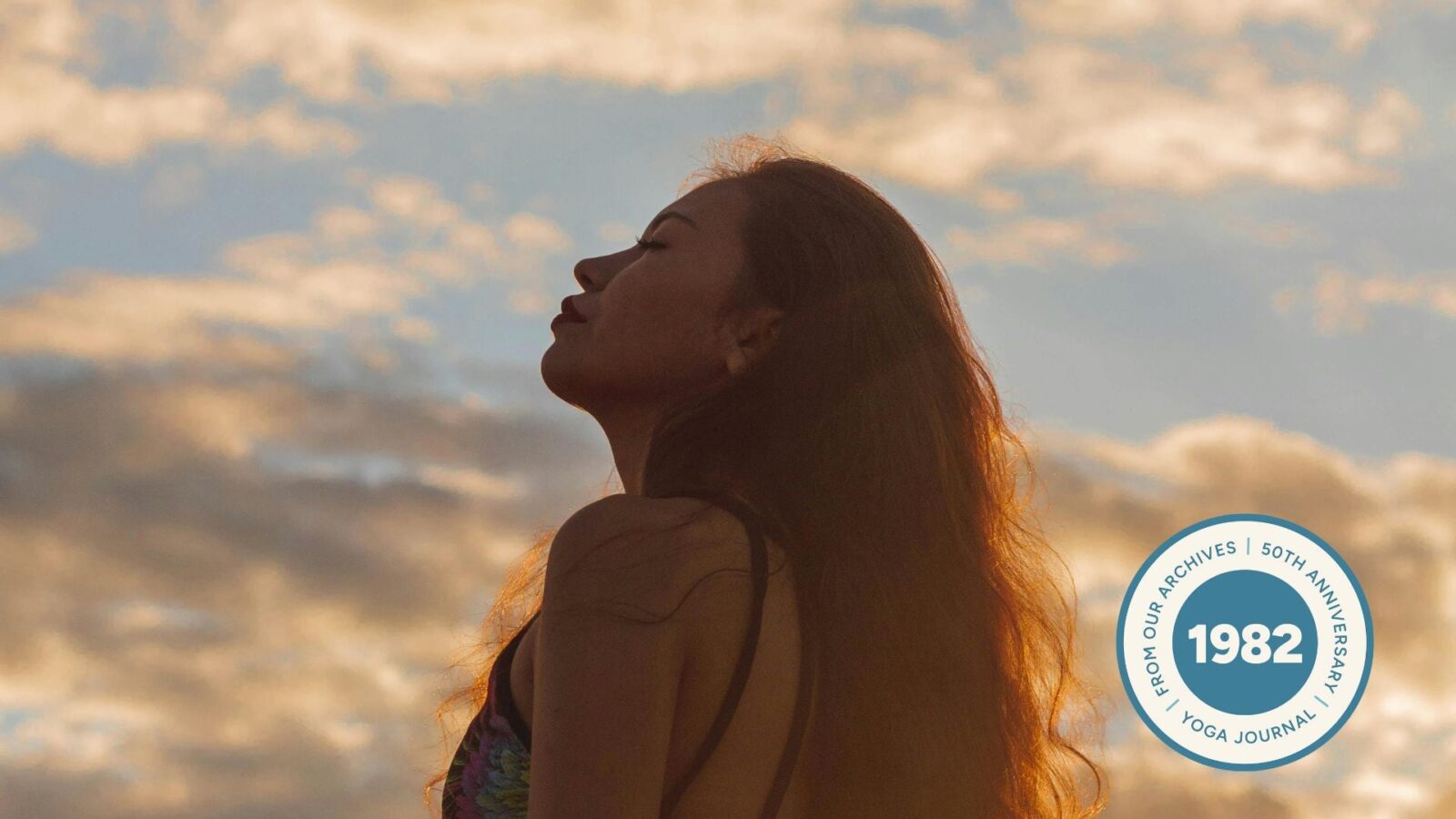 Silhouette of a woman who's standing outside during sunset with a blue-pink sky, with her eyes closed.