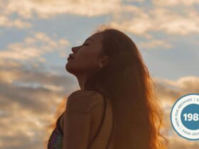 Silhouette of a woman who's standing outside during sunset with a blue-pink sky, with her eyes closed.