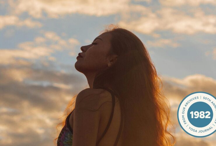 Silhouette of a woman who's standing outside during sunset with a blue-pink sky, with her eyes closed.