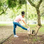 woman in park doing standing hurdler stretch to relieve L5 to S1 exercise to relieve compression