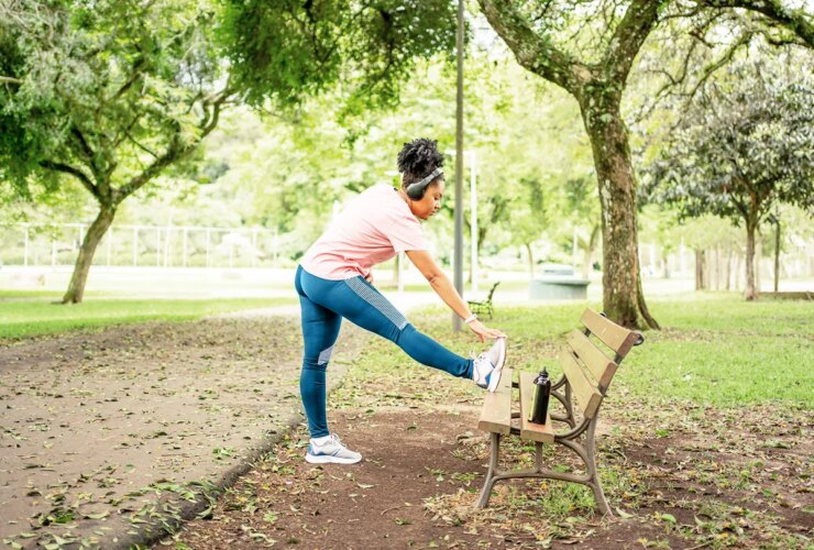 woman in park doing standing hurdler stretch to relieve L5 to S1 exercise to relieve compression