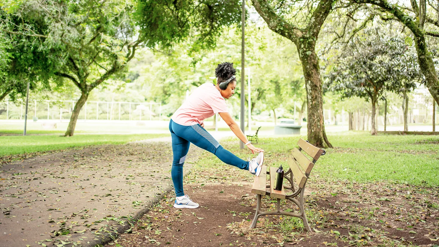woman in park doing standing hurdler stretch to relieve L5 to S1 exercise to relieve compression