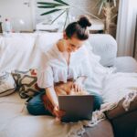 Woman sitting on couch with cat in lap looking at tablet.