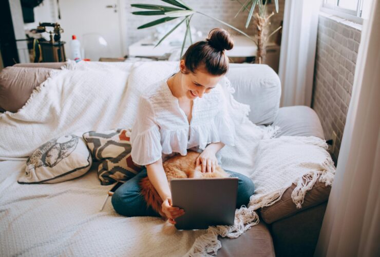 Woman sitting on couch with cat in lap looking at tablet.
