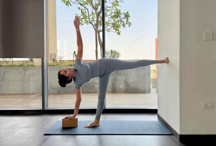 Yoga instructor Riya Davda practicing Half Moon Pose against a wall.