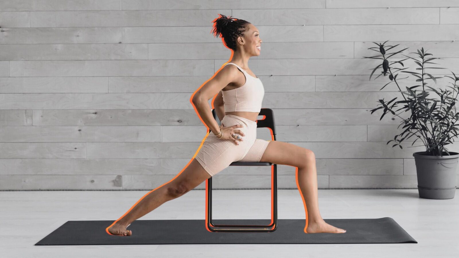 Woman practicing Warrior 2 on a chair against a black and white background of a yoga studio.