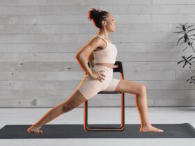 Woman practicing Warrior 2 on a chair against a black and white background of a yoga studio.