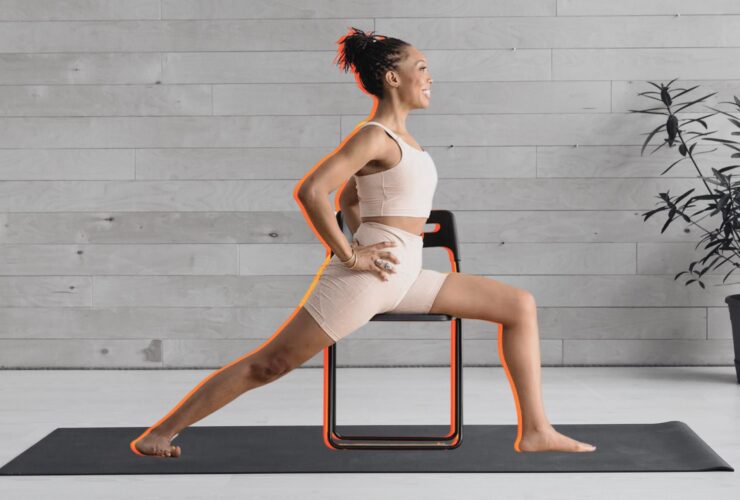 Woman practicing Warrior 2 on a chair against a black and white background of a yoga studio.