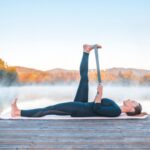 Woman practicing Reclining Hand to Big Toe Pose outdoors against a nature scene of trees.