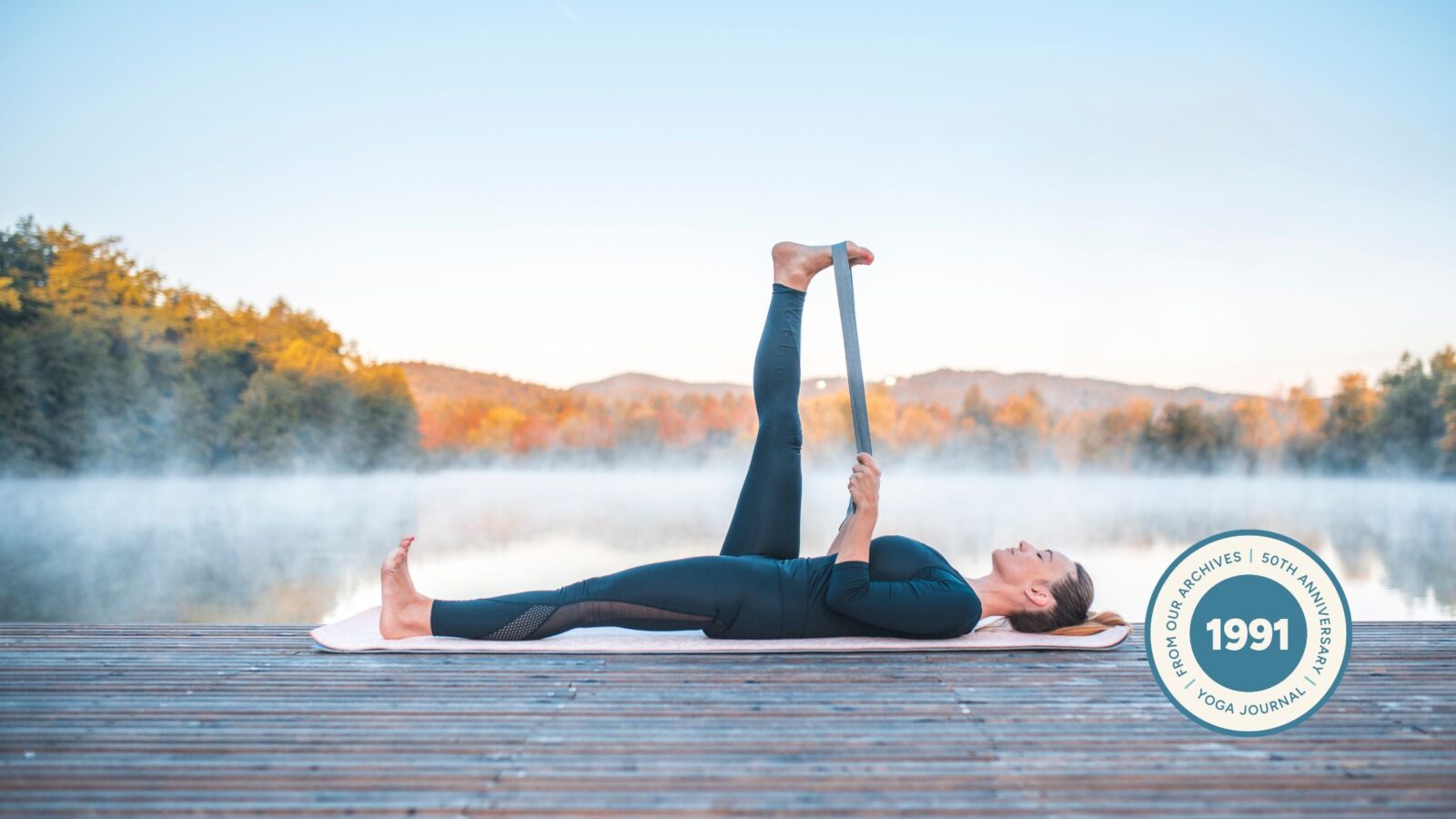 Woman practicing Reclining Hand to Big Toe Pose outdoors against a nature scene of trees.