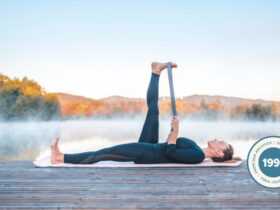Woman practicing Reclining Hand to Big Toe Pose outdoors against a nature scene of trees.