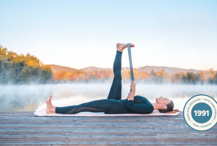 Woman practicing Reclining Hand to Big Toe Pose outdoors against a nature scene of trees.