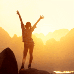 Woman hiker watching sunrise over the mountains with her arms thrown in the air