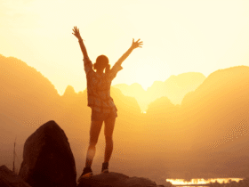 Woman hiker watching sunrise over the mountains with her arms thrown in the air
