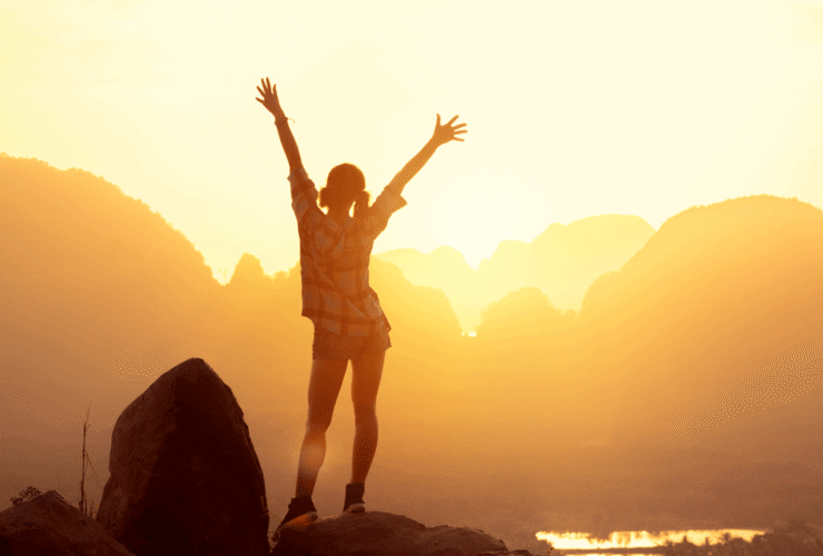 Woman hiker watching sunrise over the mountains with her arms thrown in the air