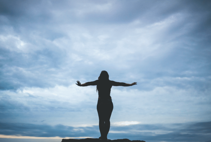 Woman silhouette standing on a cliff near a beach with dark clouds considering the weekly horoscope for November 17-23, 2024.