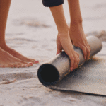 Woman standing on a beach rolling up an eco-friendly yoga mats on the sand