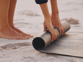 Woman standing on a beach rolling up an eco-friendly yoga mats on the sand