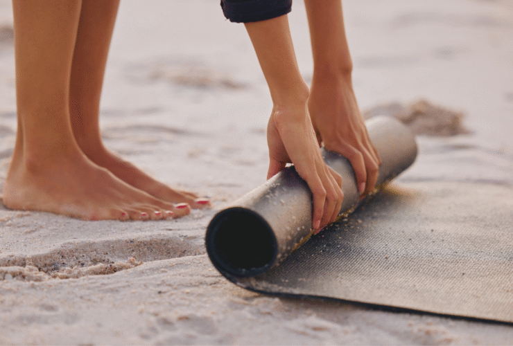 Woman standing on a beach rolling up an eco-friendly yoga mats on the sand