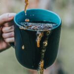 Image of a person's hand holding a cup of coffee, with liquid splashing over its edges.