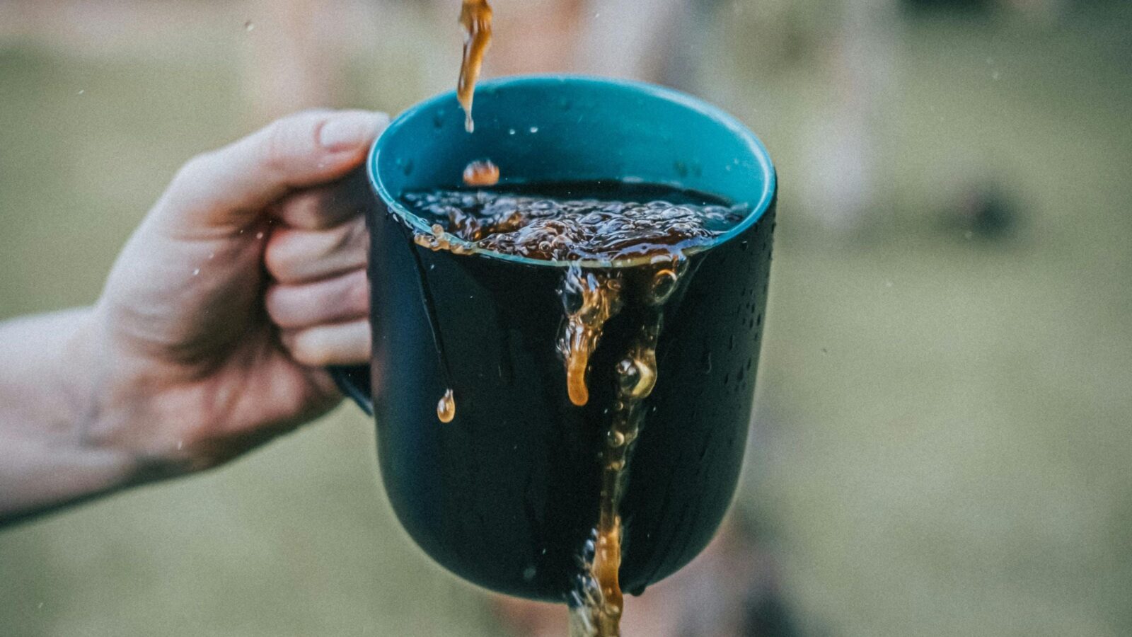 Image of a person's hand holding a cup of coffee, with liquid splashing over its edges.
