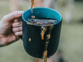 Image of a person's hand holding a cup of coffee, with liquid splashing over its edges.