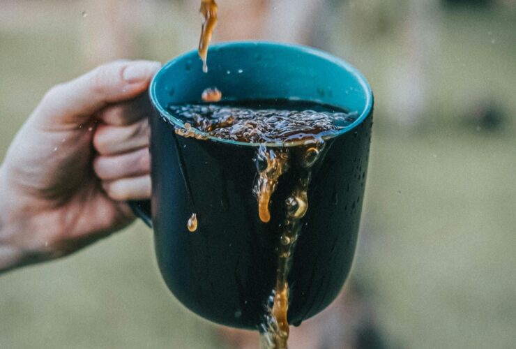 Image of a person's hand holding a cup of coffee, with liquid splashing over its edges.